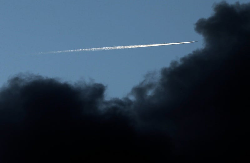 Aircraft leaving clear contrail against a cloudy dark background